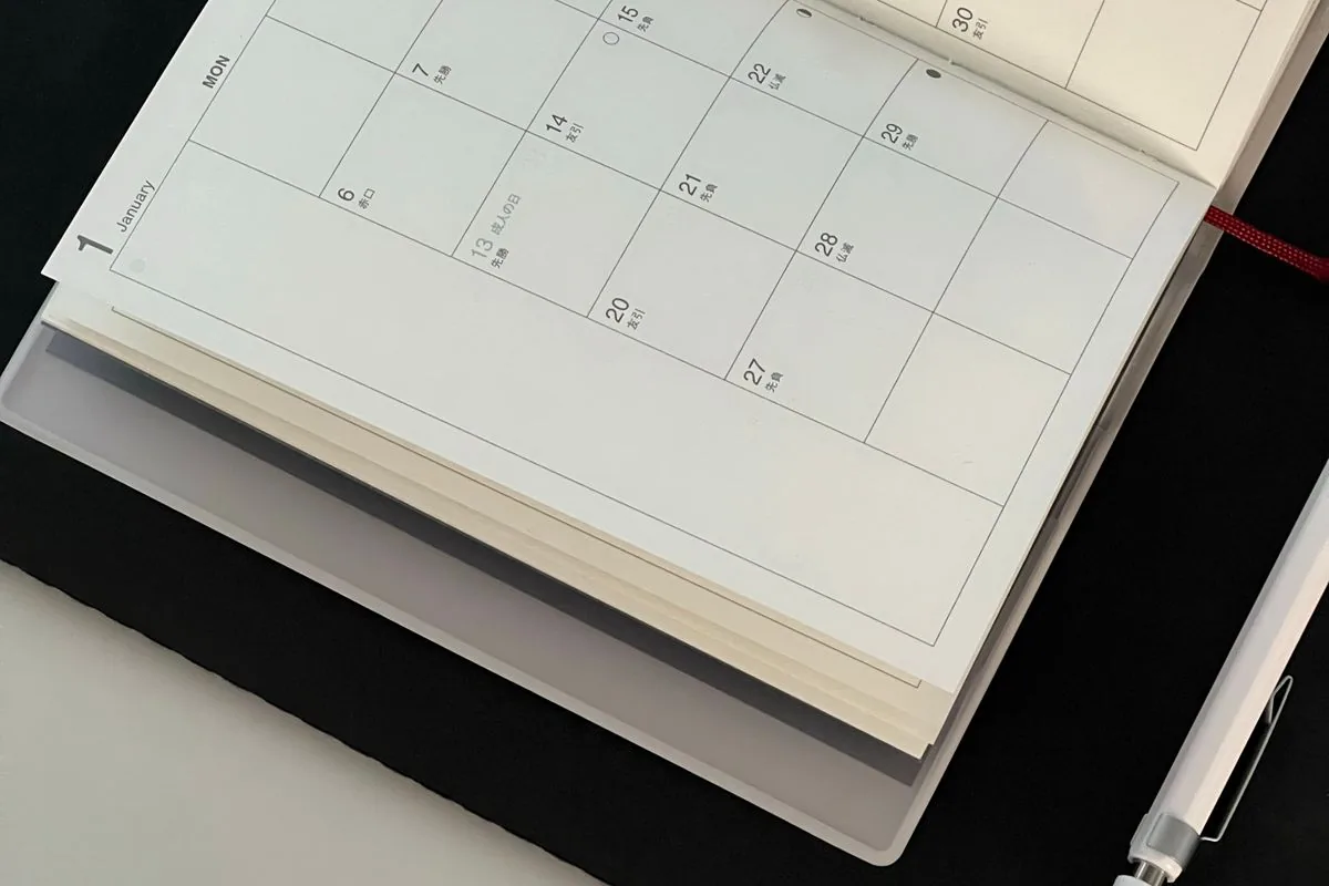 An open monthly calendar and pen on a dark desktop.
