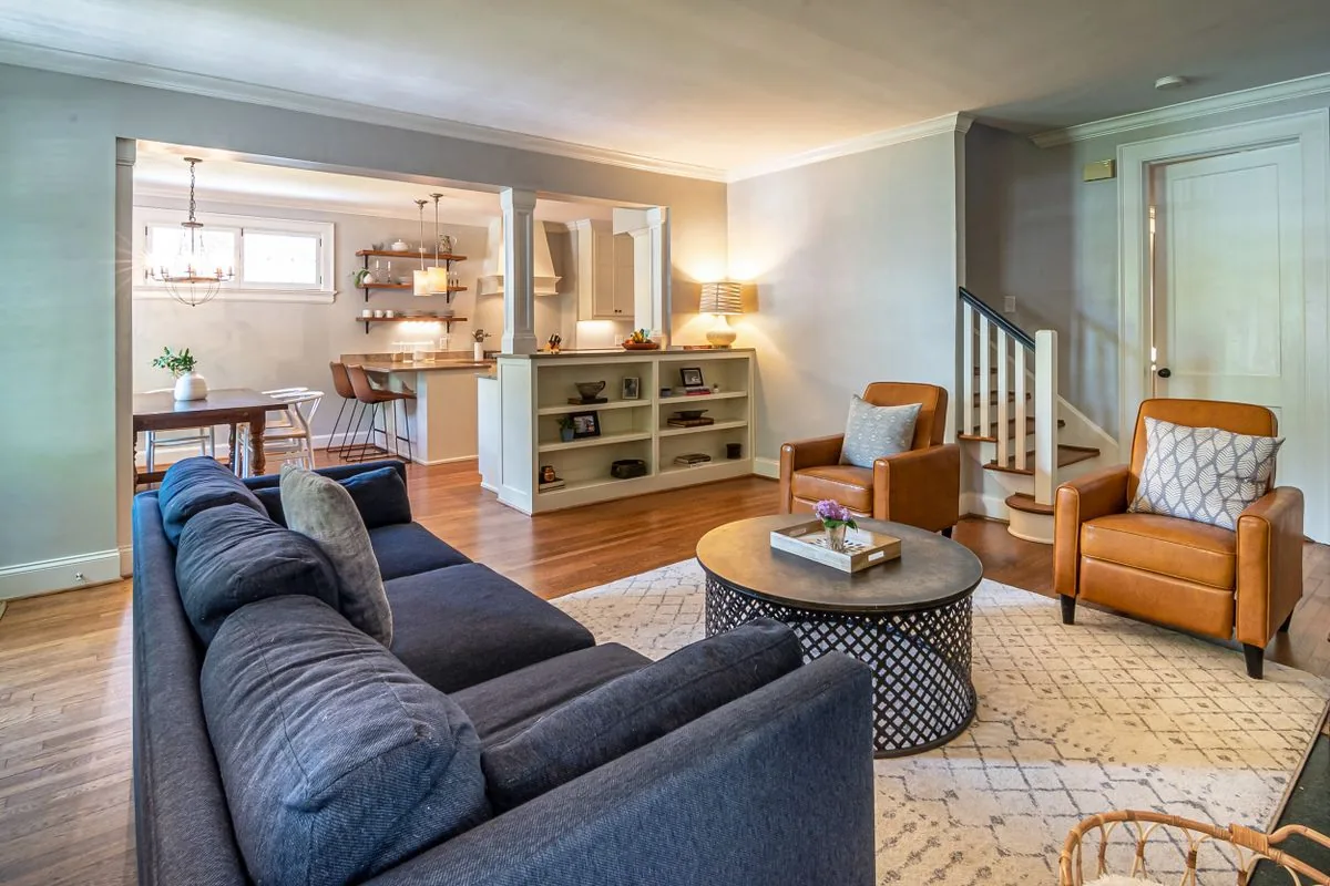 A blue sofa and warm wooden furniture in a light-filled living room opening onto a kitchen.