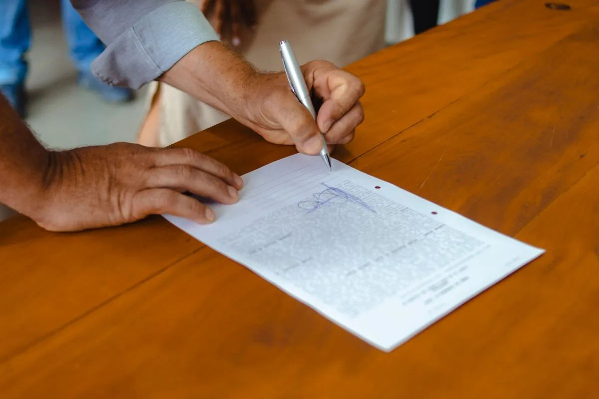 A person writing on a document at a wooden table.