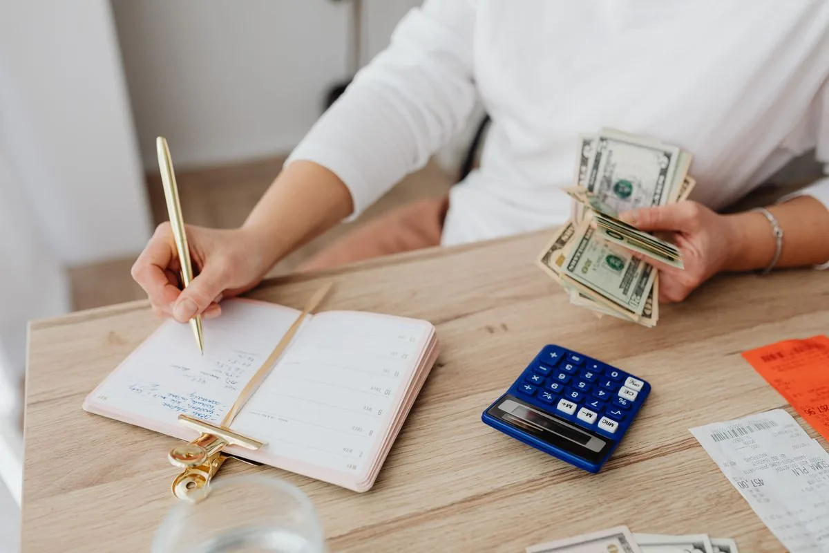 A person recording household expenses in a planner beside a blue calculator.