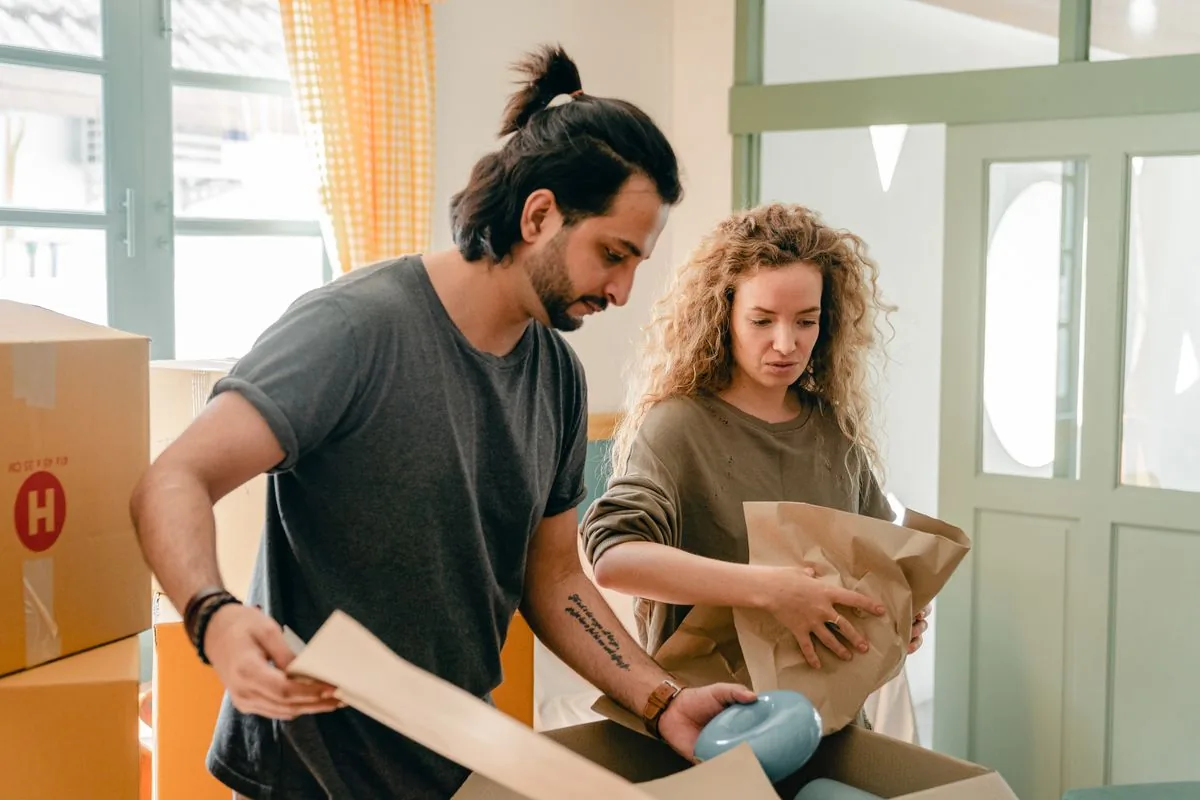 Two people wrapping household belongings and packing cardboard moving boxes.