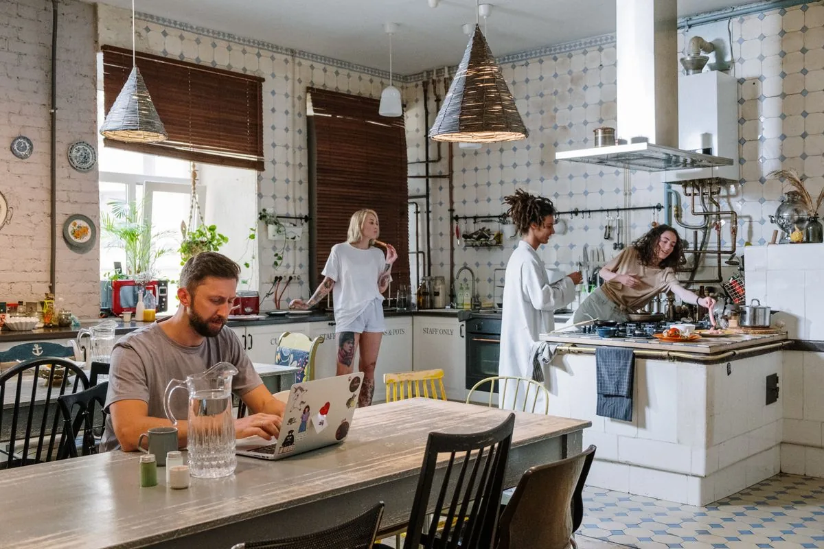 Housemates sharing a kitchen, with one person working at the dining table.