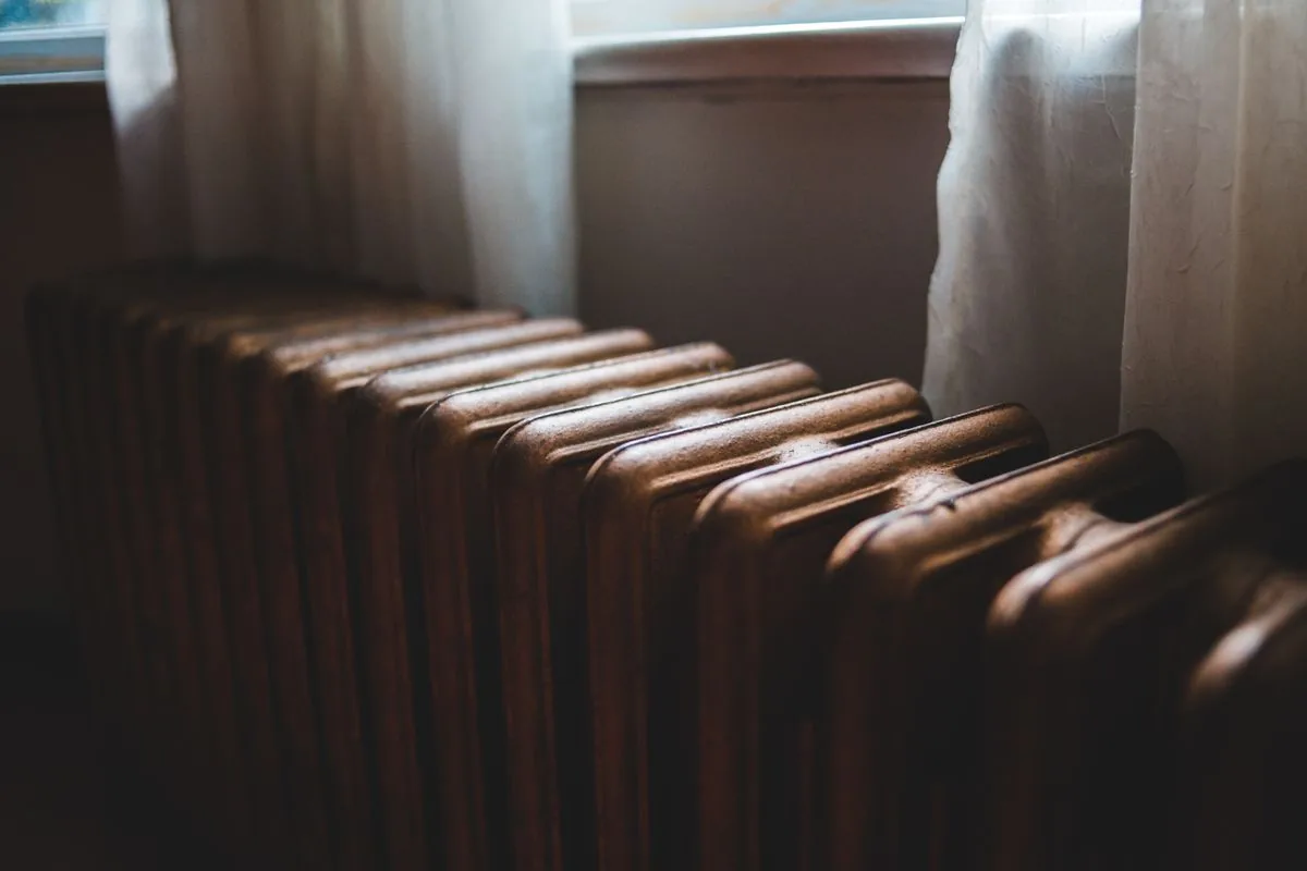Daylight falling across a cast-iron radiator beneath a curtained window.